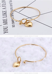 Detailed close-up of golden heart pendant on a minimalist stainless steel open bangle