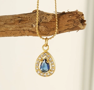 Detail of water drop blue zircon pendant on golden stainless steel chain over wood
