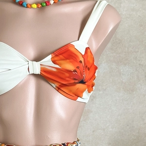 Close-up of a white bikini top featuring vibrant orange floral prints and ruched center detail