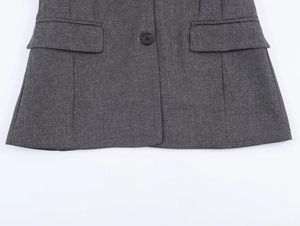 Dettaglio macro della trama del blazer grigio scuro con bottone nero e tasca a pattina