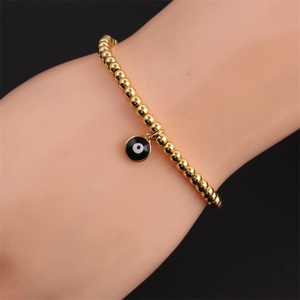 Close-up of gold beaded elastic bracelet with black and white evil eye enamel charm