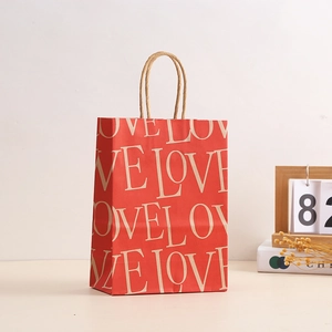 Red Valentine paper gift bag with LOVE pattern and twisted paper handles on a warm desk