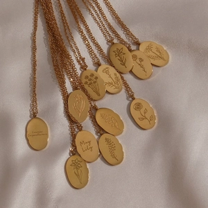 Golden stainless steel oval birth flower necklace displayed on white silk background