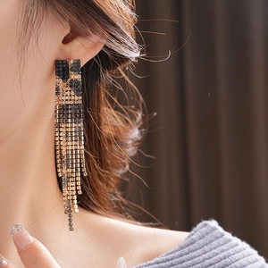 Close-up of elegant long tassel earrings with black and gold rhinestones on a model