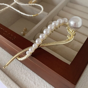Detail of elegant gold metal hair clip with gradient oversized pearls on a wooden box