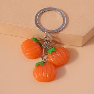 Close-up of orange pumpkin keychains with green stems on beige geometric background