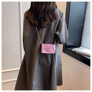 Pink mini crossbody bag with crocodile texture and silver chain on a model in a trench coat