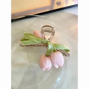 Detail of fabric tulip floral hair claw with green ribbon bow on a glass tray