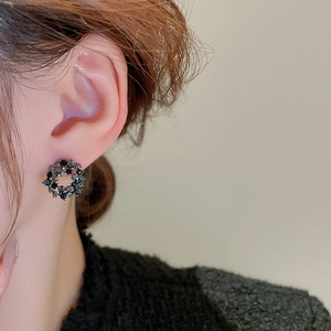 Close-up of black geometric circle earrings with dark crystals worn by a model