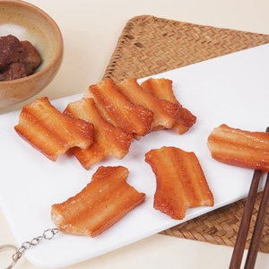 Realistic PVC braised pork belly keychain with oily texture and metal ring on white tray