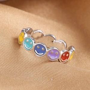 Colorful enamel smiley face ring in silver-tone finish on elegant gold satin background
