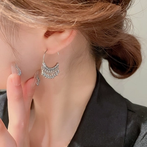 Detail of silver C-shaped metal tassel earrings with water drop charms on a female model