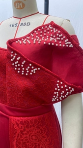 Detail des roten Spitzenkleids mit weißen Perlenbestickungen und Satin-Stoffstruktur
