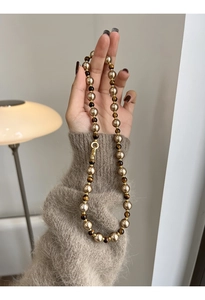 Détail d'un collier de perles plaquées or et pierres œil de tigre tenu par un mannequin