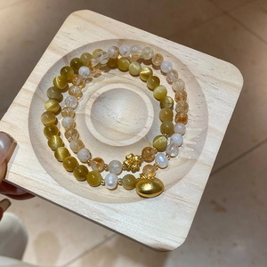 Détail de bracelets en œil de tigre et perles avec pendentifs fleur dorés sur bois