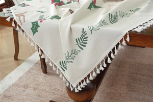 Close-up of Christmas tablecloth featuring green leaves, red berries, and white tassels