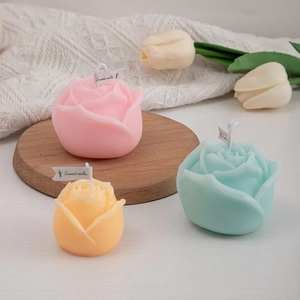 Three rose-shaped scented candles in pink, blue, and yellow with elegant knit background