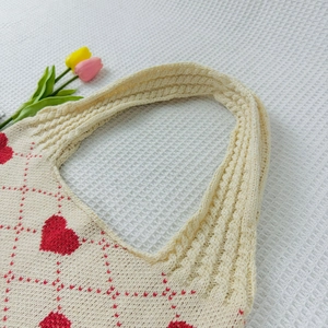 Close-up of cream knit tote bag featuring red heart patterns on white textured fabric
