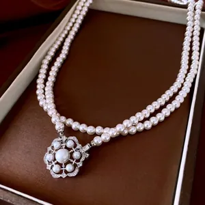 Double-layer white pearl necklace featuring a floral diamond pendant on a brown tray
