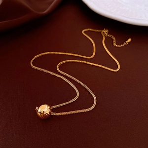 Detailed macro shot of an 18K gold-plated ball pendant necklace on rich brown texture