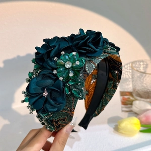Close-up of a wide dark green headband with silk flowers and sparkling rhinestones