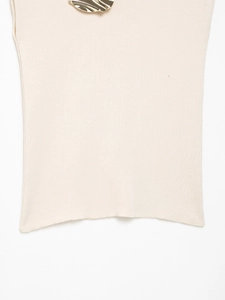 Detailed close-up of beige knit top with stylish golden wave metal neck decoration