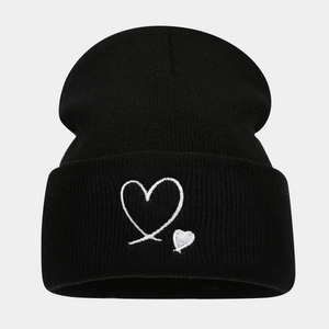 Détail d'un bonnet en maille noire avec broderie de deux cœurs blancs sur le revers