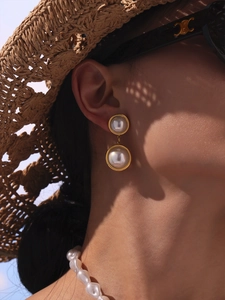 Close-up of elegant double pearl earrings with golden metal frames on a female model