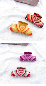 Close-up of colorful acrylic heart hair claws in retro patterns on white fabric background