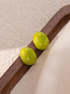 Close-up of green marble textured oval earrings displayed on a dark wooden tray