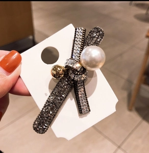 Bow hair clip with dark rhinestones and white pearls on a display card held by hand