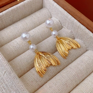 Detail of gold mermaid tail earrings with double pearls inside a beige jewelry box