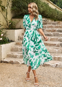 Détail de robe longue blanche à col en V, imprimé vert et manches bouffantes dans un jardin