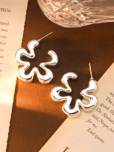 Macro shot of silver C-shaped wave flower acrylic earrings on a vintage paper backdrop