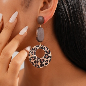 Close-up of leopard print acrylic and wood drop earrings worn by a model for a retro look