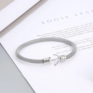 Polished silver anchor cable bangle with intricate woven mesh texture on a book