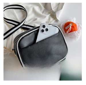 Detail of the back pocket on a black camera-shaped bag with striped strap and phone storage