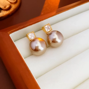 Macro shot of gold-plated stud earrings with square zircon and large champagne pearl