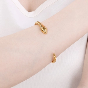 Close-up of golden snake-shaped open bangle with intricate engraved patterns on model's wrist