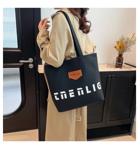 Detail of black canvas tote bag with ENERLIG lettering worn by model in beige coat