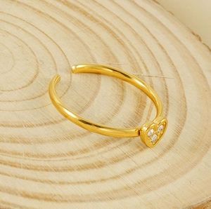 Macro detail of gold heart ring with three tiny zircons on a wooden background
