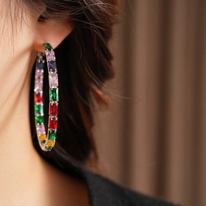 Close-up of silver hoop earring with multi-color rectangular zircon stones on model