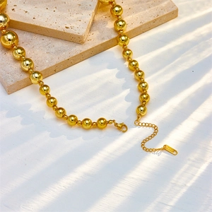 Minimalist golden stainless steel bead necklace with lobster clasp on beige stone slab
