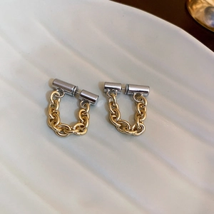 Detail of two-tone gold chain and silver cylindrical metal drop earrings on white tray