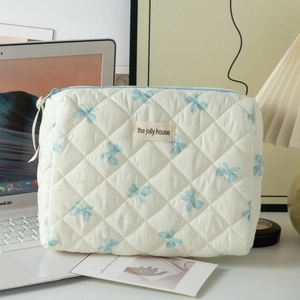Détail de trousse de maquillage blanche matelassée avec nœuds bleus et étiquette