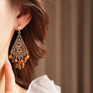Close-up of ethnic gold zircon earrings with tiger eye beads on a female model