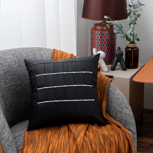 Close-up of black leather cushion with white stitching on a grey chair with orange throw