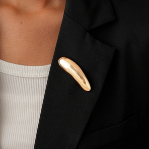 Detail of a shiny gold organic curved brooch on a black suit lapel with mirror finish