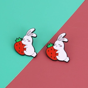 Detail of two white rabbit enamel pins holding red strawberries on green background