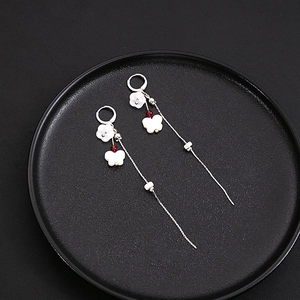 Detail of silver drop earrings with white flower and butterfly tassels on a black tray